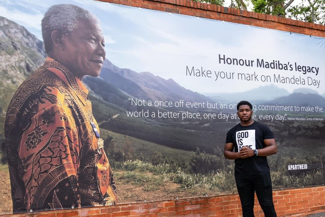 Emiere Scaife, founder of Black Boys 2 Men, at the Apartheid Museum in front of a Mandela Day banner of Nelson Mandela